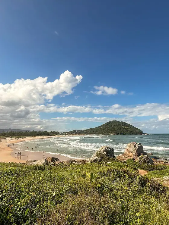 Praia com morro ao fundo e pedras na beira do mar, no litoral de Garopaba